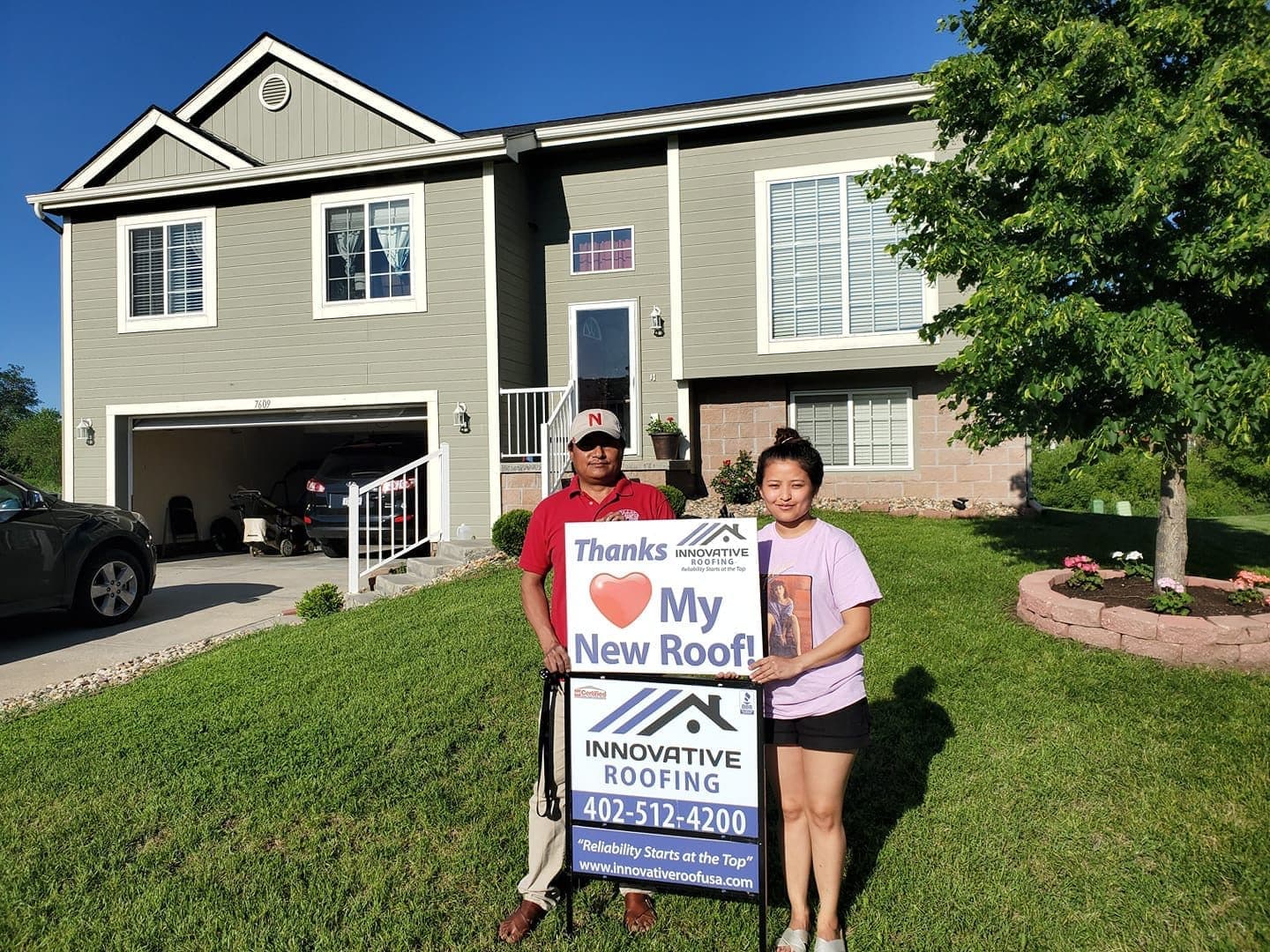 Homeowners holding Innovative Roofing thank-you and yard signs in front of their home after a roof project