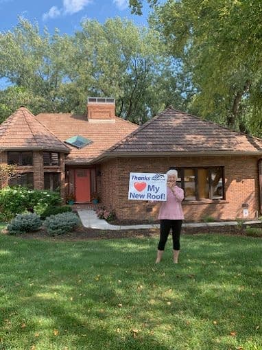Homeowner holding an Innovative Roofing thank-you sign in front of their home