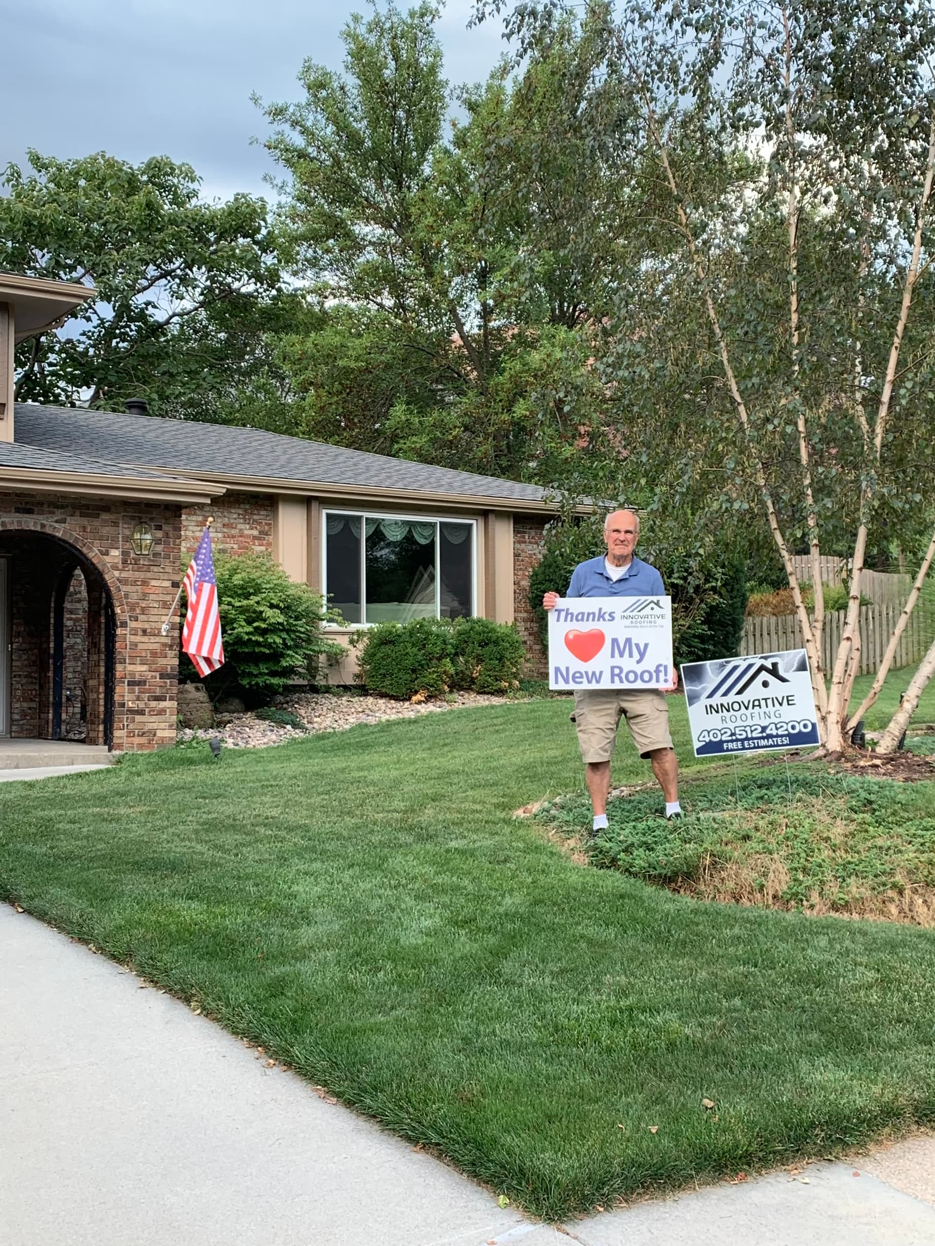 Homeowner on the lawn holding a Thanks Innovative Roofing My New Roof sign next to a free-estimate yard sign