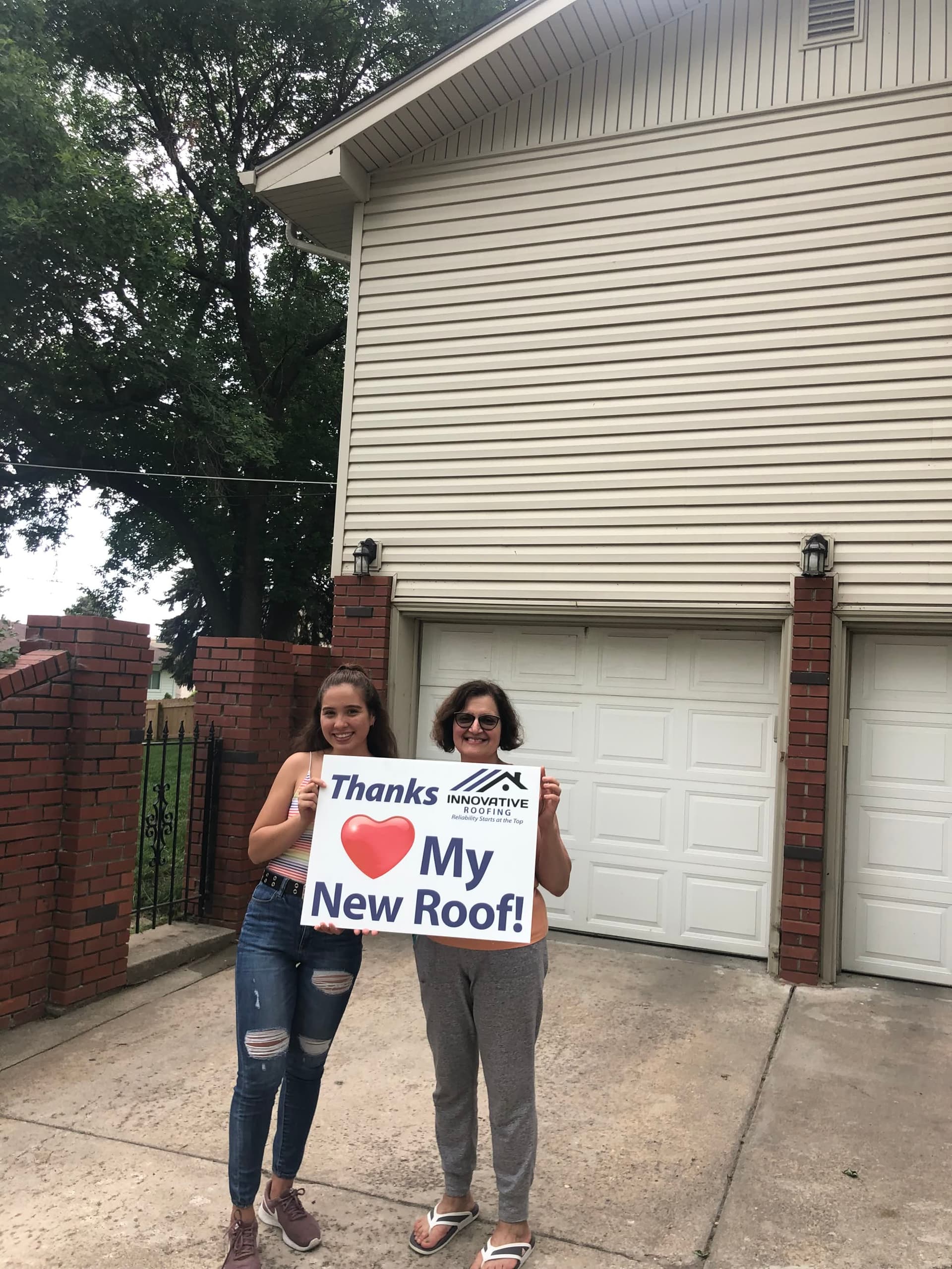 Two homeowners smiling on their driveway holding a Thanks Innovative Roofing My New Roof sign