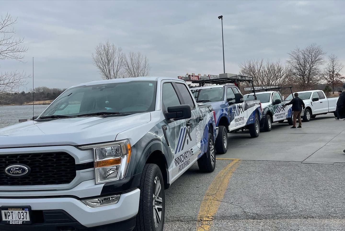 Line of white Innovative Roofing Ford F-150 service trucks with company wraps parked outdoors