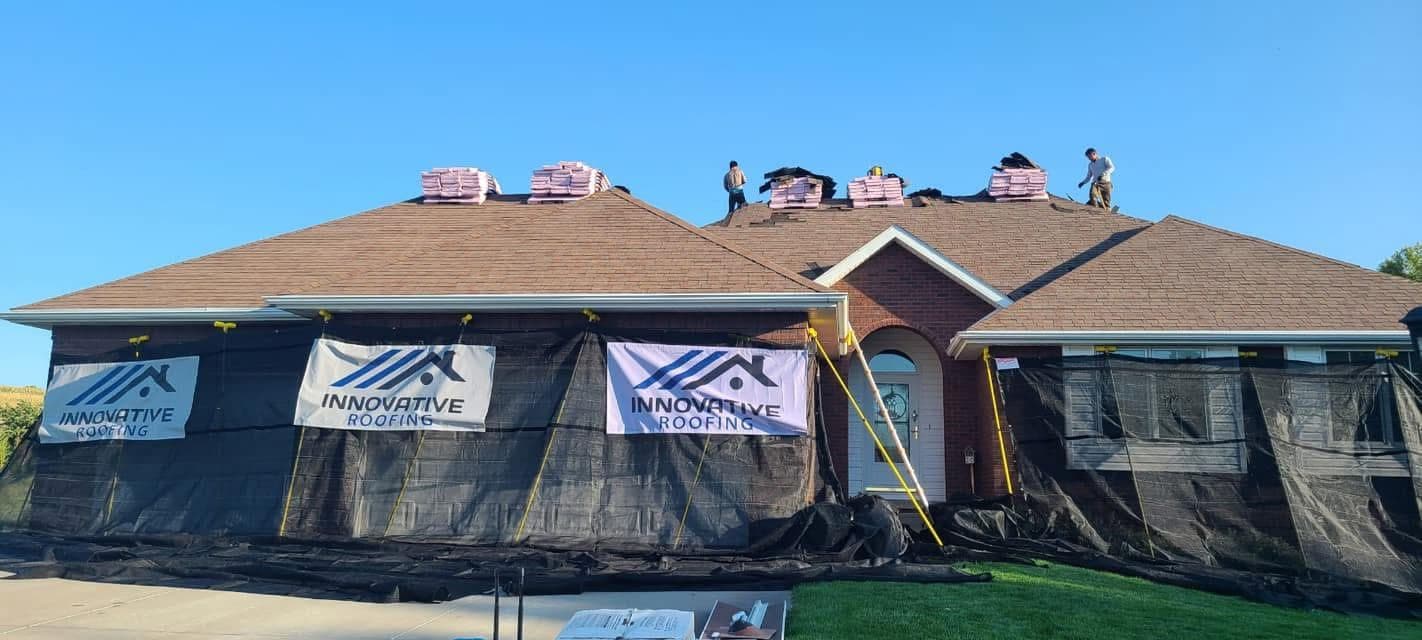Red brick ranch mid roof replacement with crew on the roof and Innovative Roofing banners on debris netting