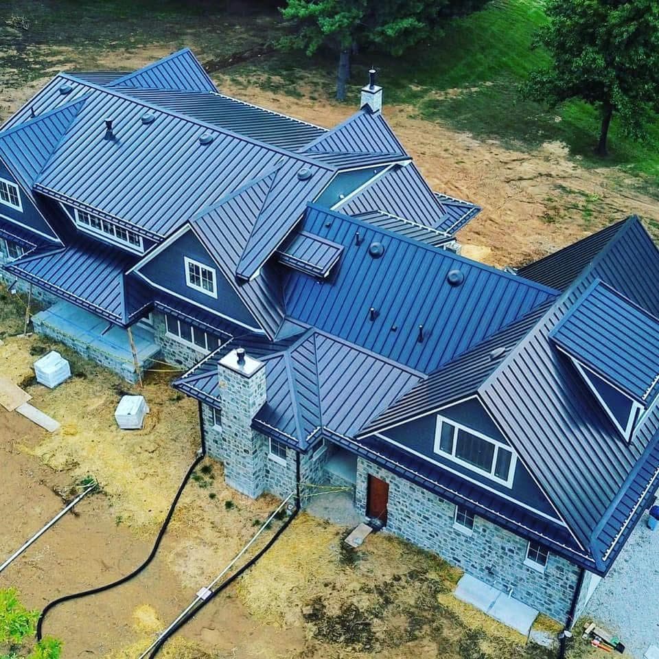 Aerial view of a large home with a complex dark standing-seam metal roof and stone masonry accents