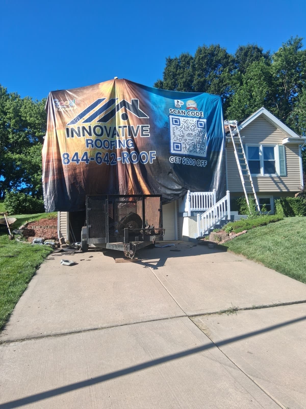 Single-story beige home with a large Innovative Roofing job-site banner, company trailer in the driveway, and ladder on the roof during an active project