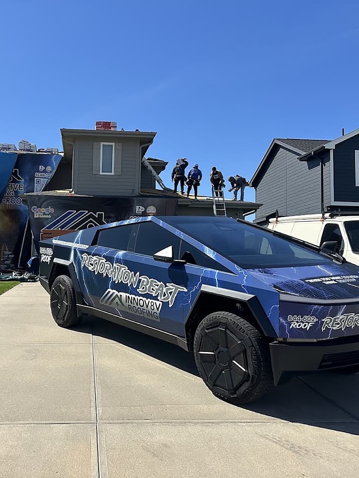 Side view of the Restoration Beast Cybertruck at a roof replacement with crew working on the roof behind it