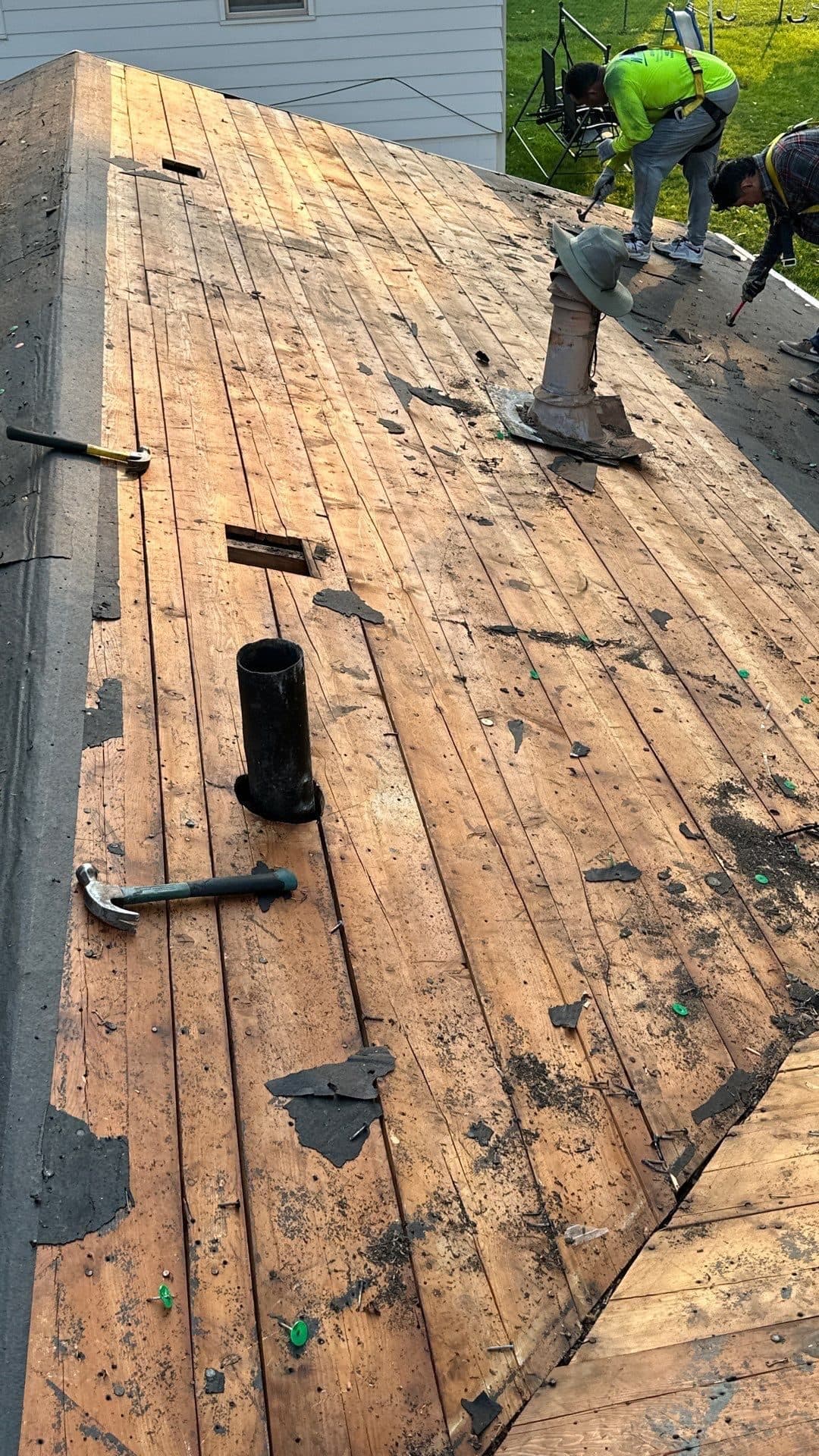Roofing crew tearing off old shingles to expose wood decking during a residential roof replacement