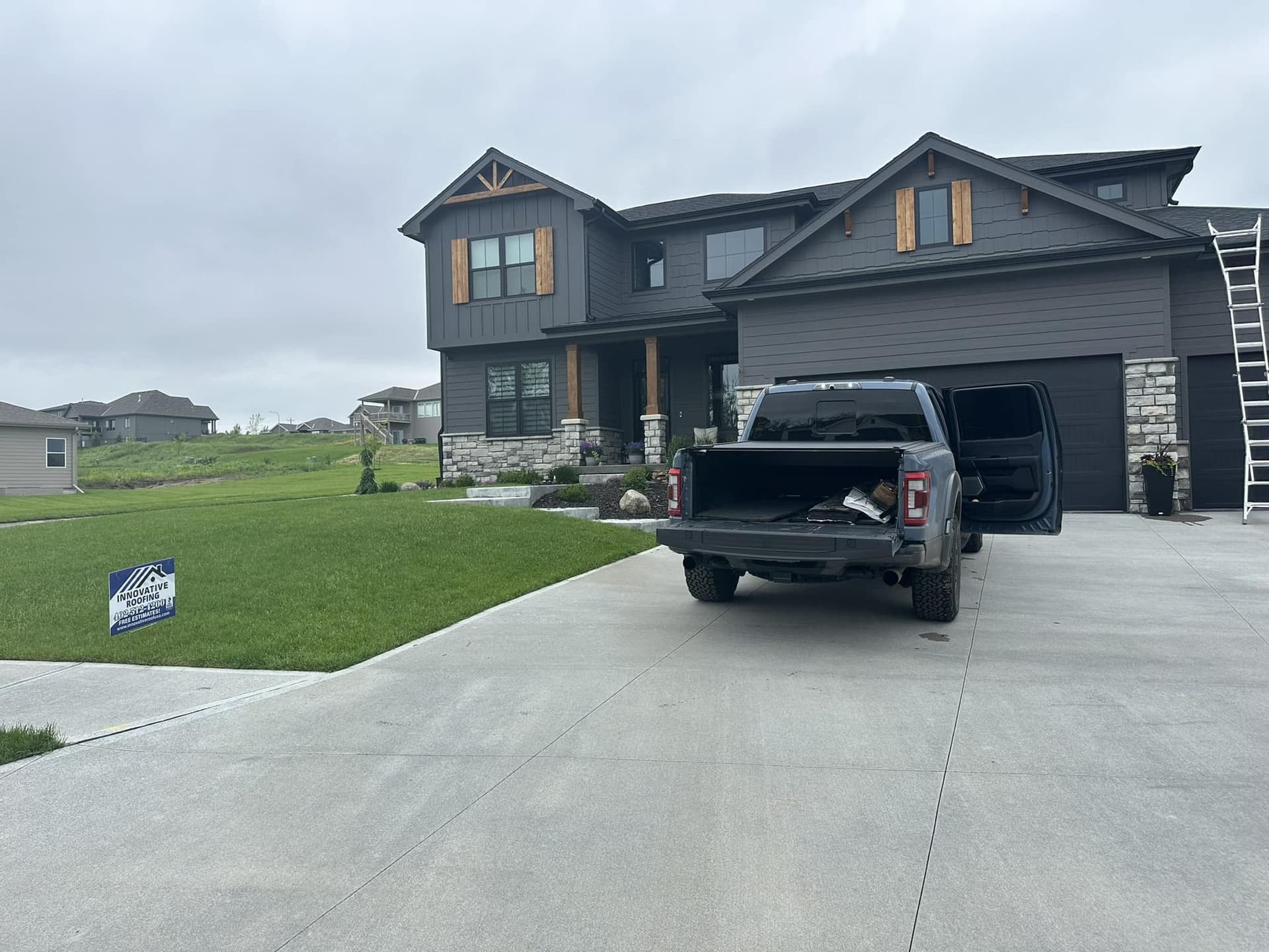 Dark gray sided home with Innovative Roofing yard sign, work truck in the driveway, and ladder against the house