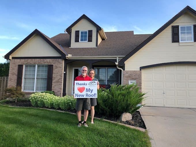 Couple smiling on their lawn holding a Thanks Innovative Roofing My New Roof sign