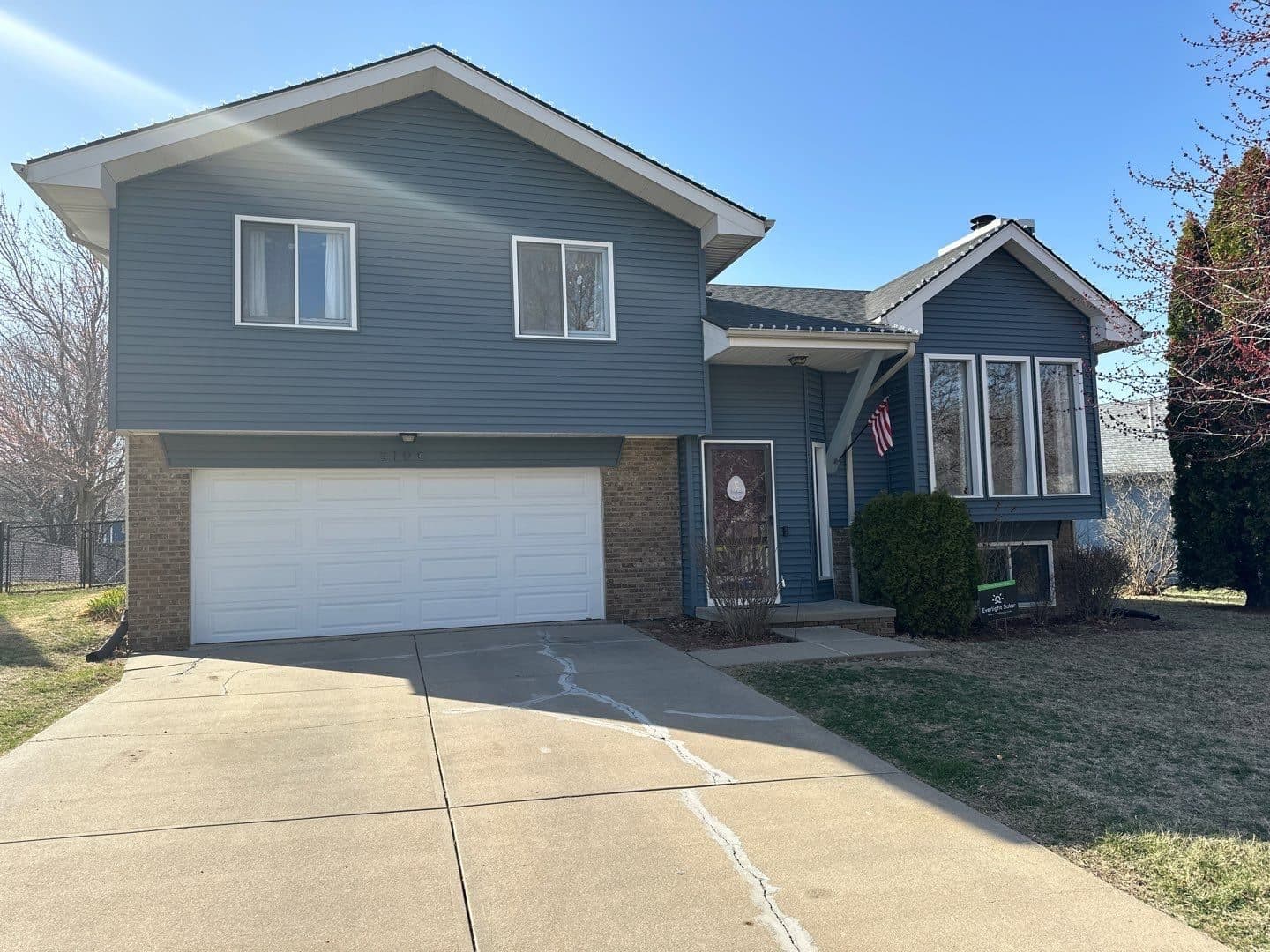 Front of a two-story light blue home with a white two-car garage and finished roof