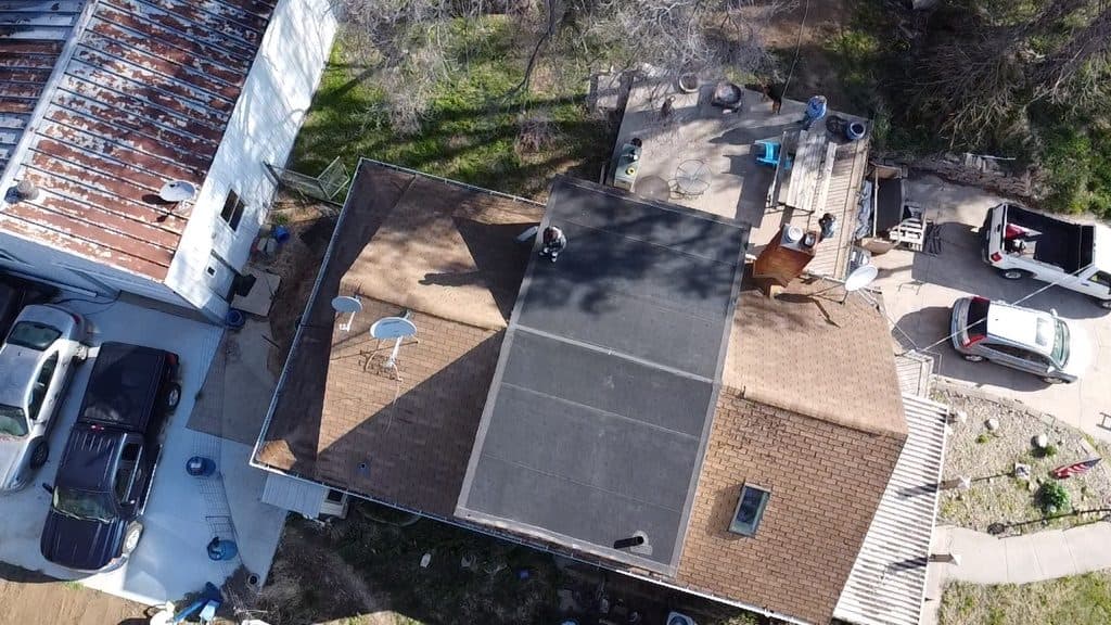 Aerial view of a home during roofing with debris and equipment on the lawn