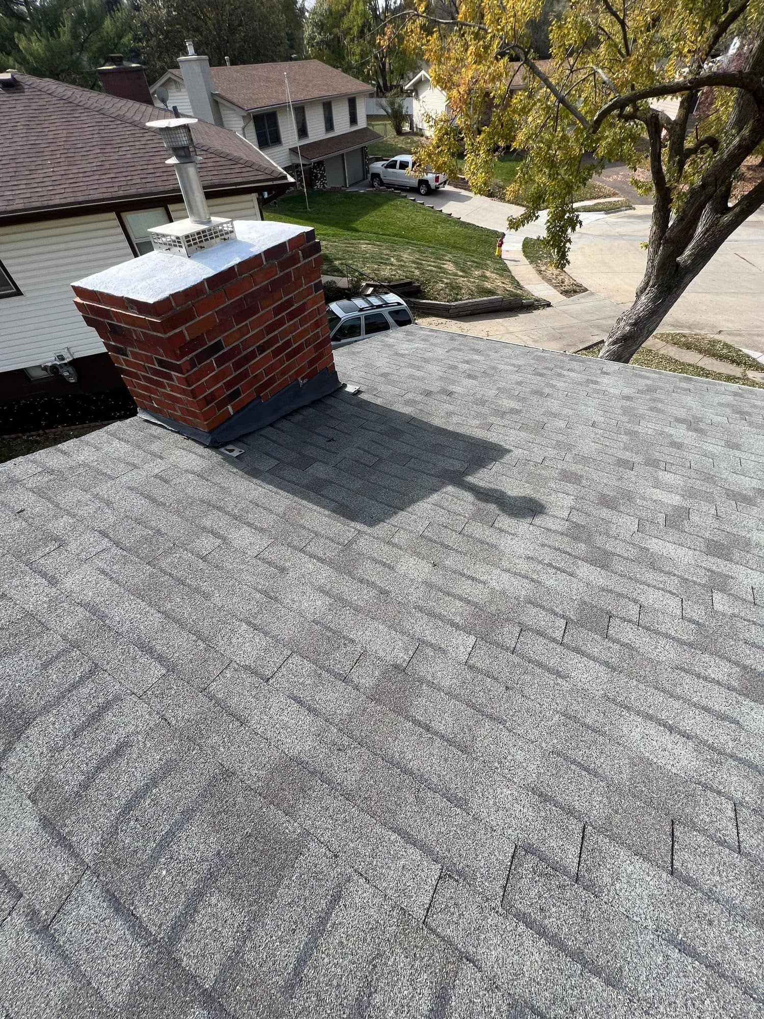 Roof corner meeting a brick chimney with trees and neighboring homes below