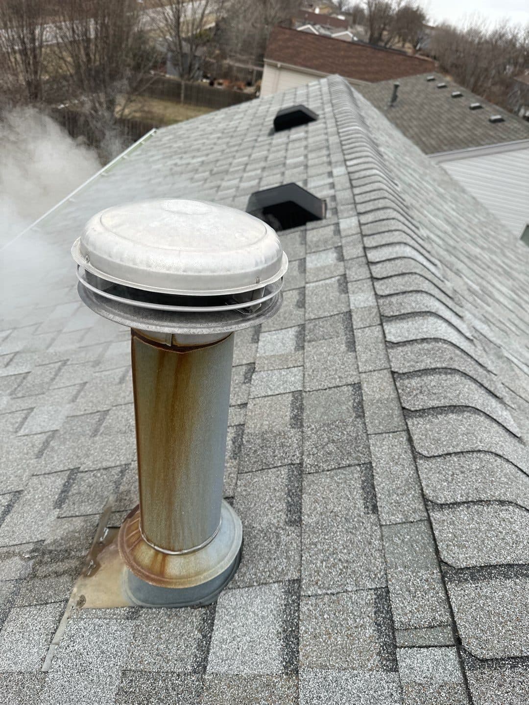 Silver cylindrical roof vent installed on gray architectural shingles