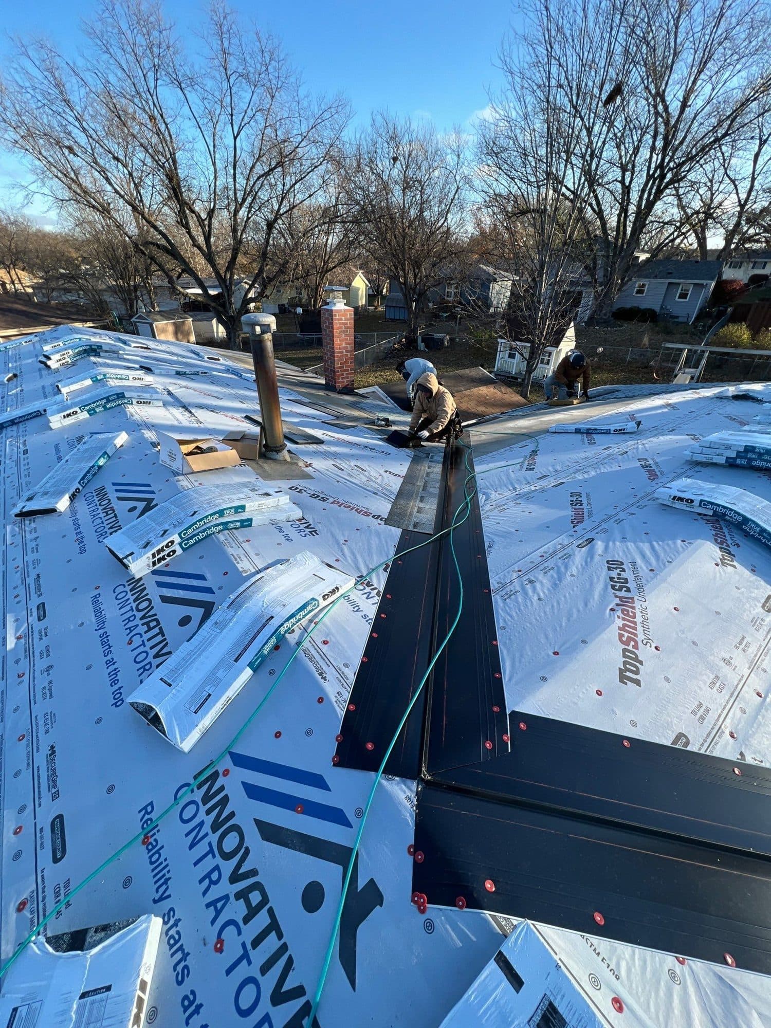 Roof replacement with Innovative Roofing branded blue underlayment and a crew member in the distance
