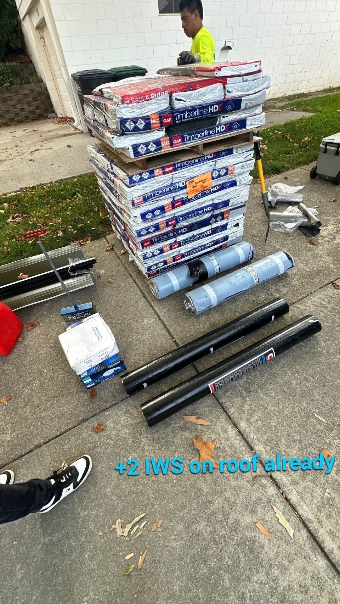 Stacks of new shingle bundles and supplies staged on a driveway next to a work vehicle