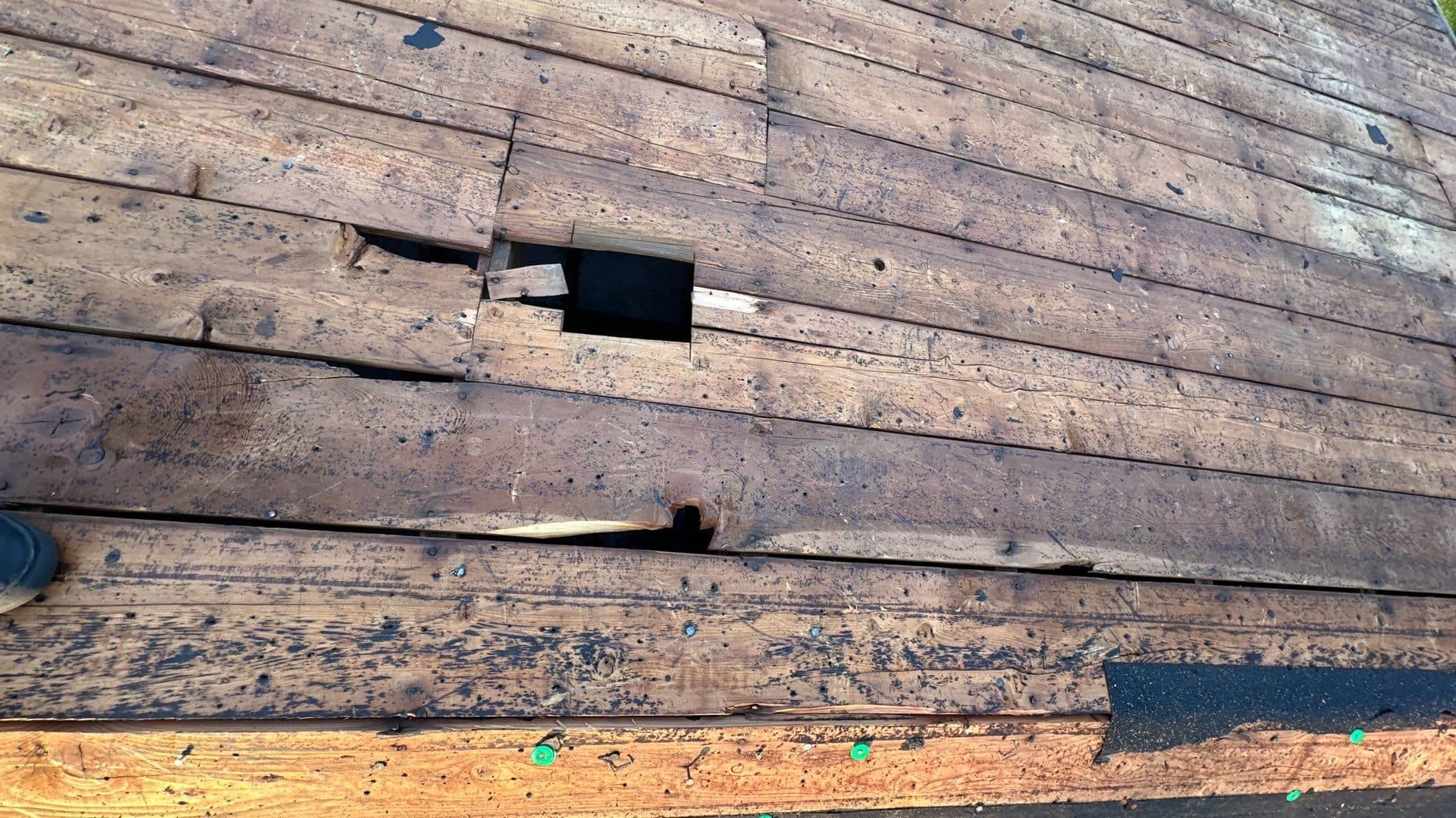 Weathered wooden roof decking with a hole exposed during inspection