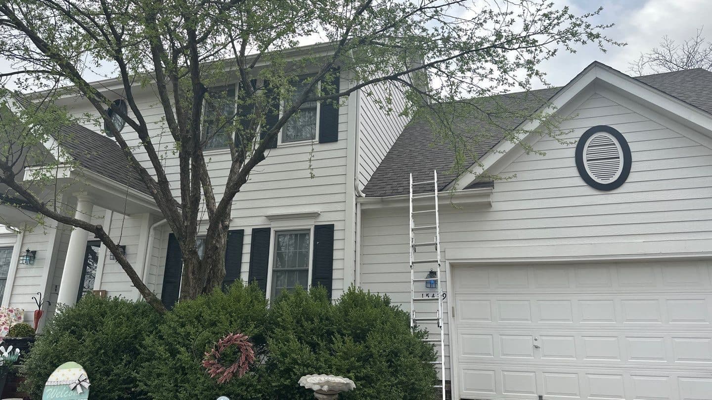 Large white multi-gable home with a ladder against the side during roofing work