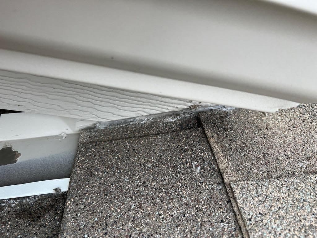 Roof edge showing white metal drip edge under new shingles