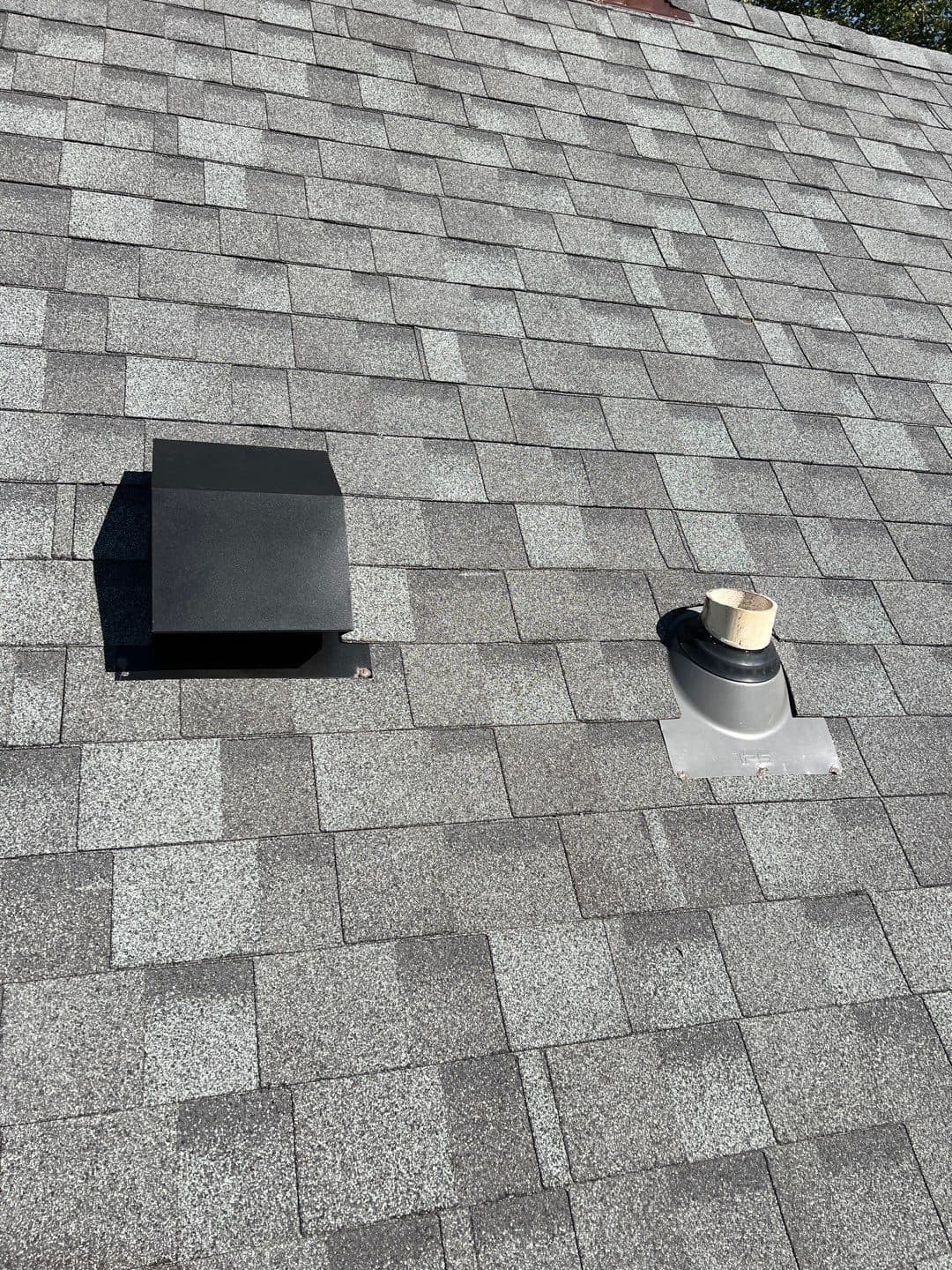 Top-down view of finished gray shingles with a square roof vent and pipe boot