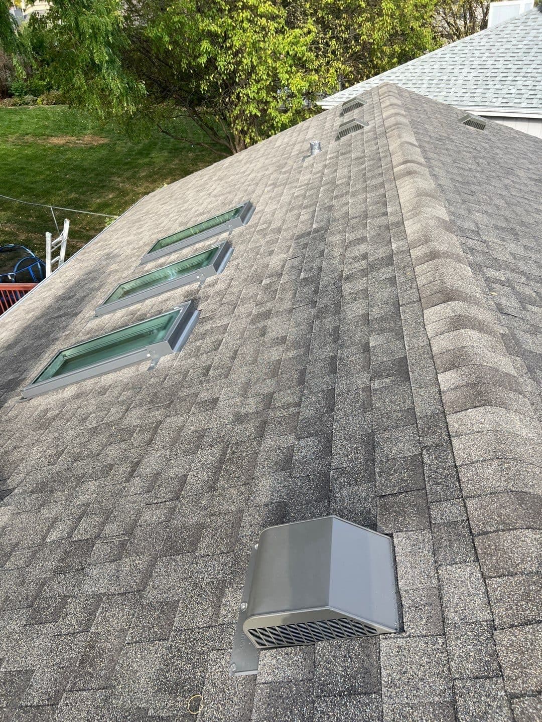 Wide view of a finished gray shingle roof with multiple skylights and a roof vent