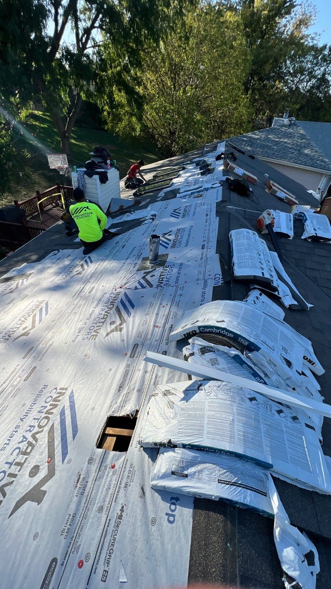 Sloped roof mid-install with blue underlayment and a crew member in a high-visibility shirt