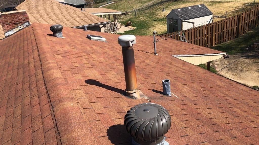 Wide view across a completed shingle roof with vent and chimney under clear sky