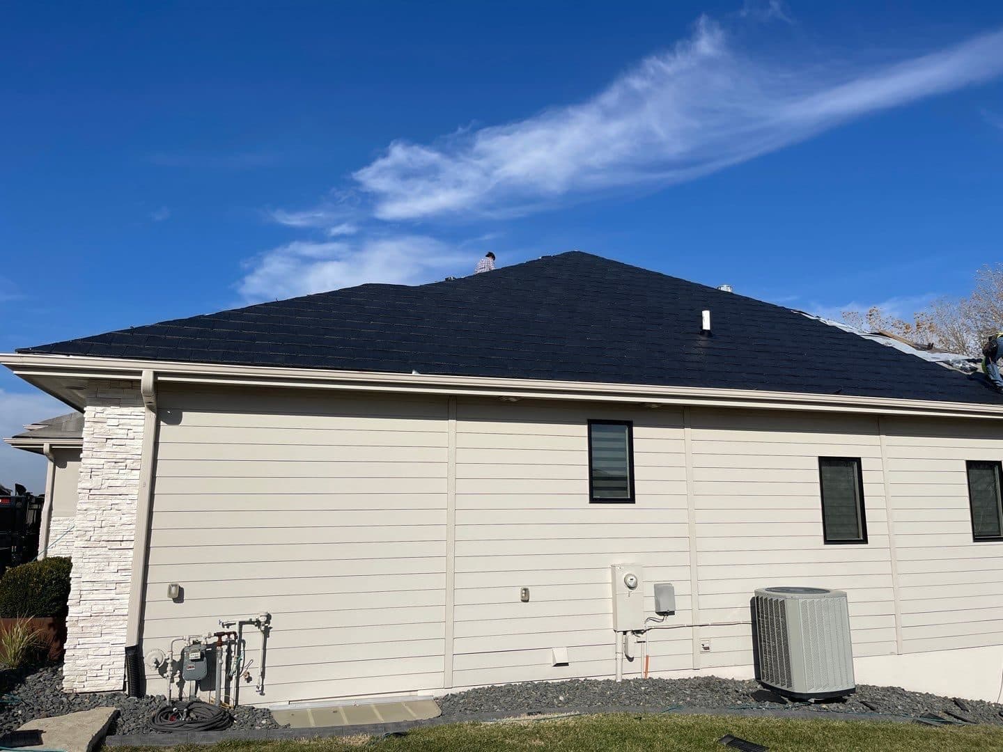 Side and back of a beige home with a clean new dark gray roof