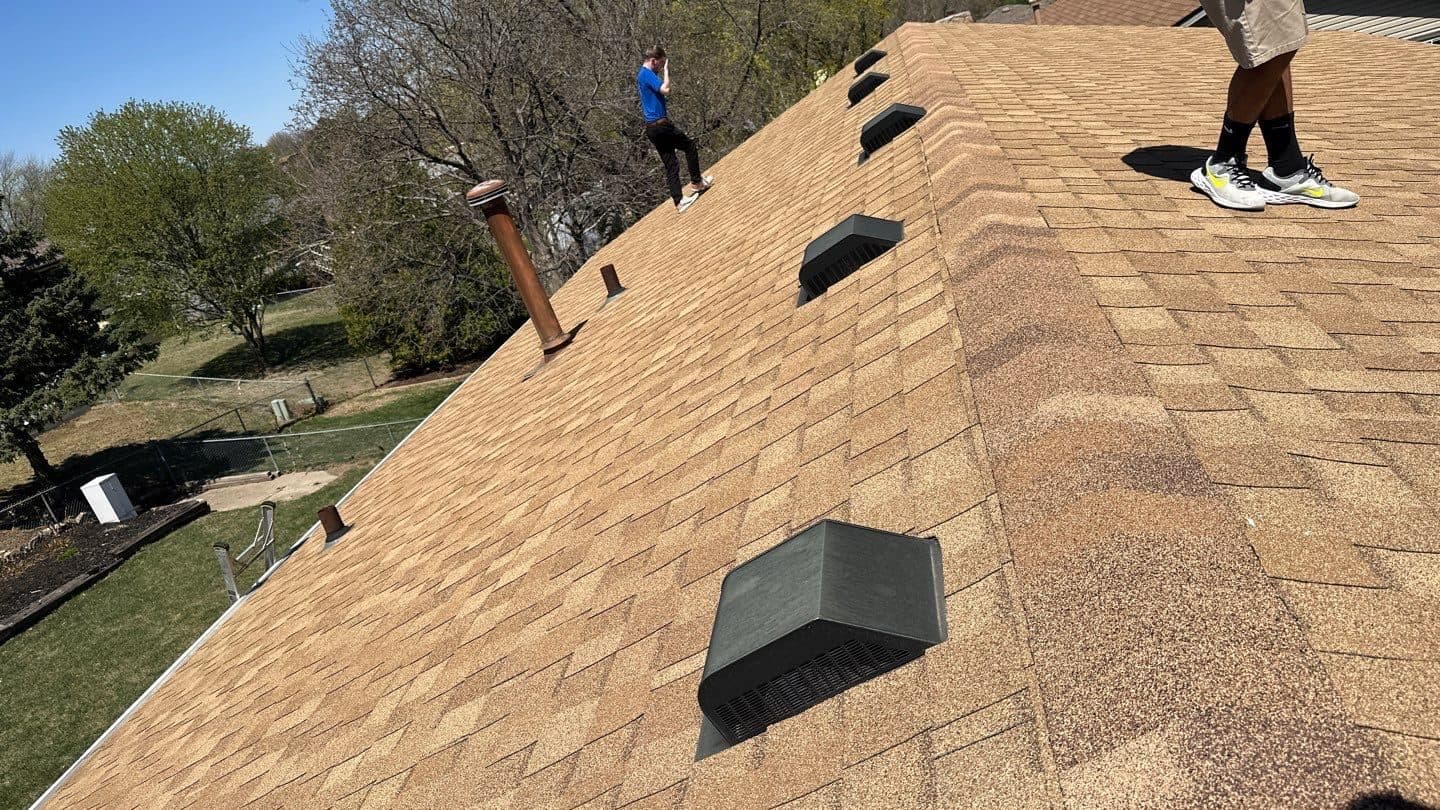 Wide view of a large home with multiple roofers working a tan shingle roof
