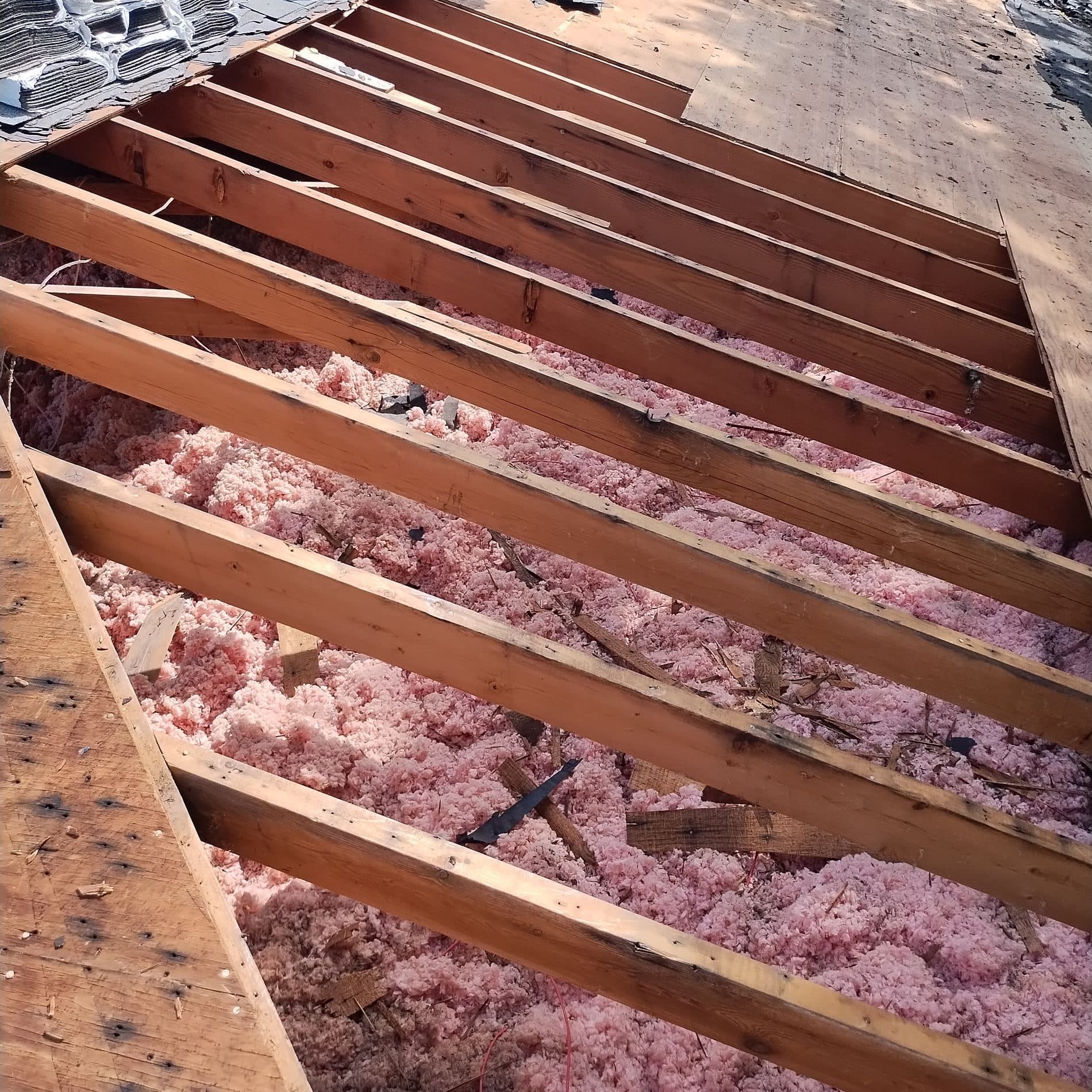 Attic view of new roof rafters installed above pink insulation during a structural repair