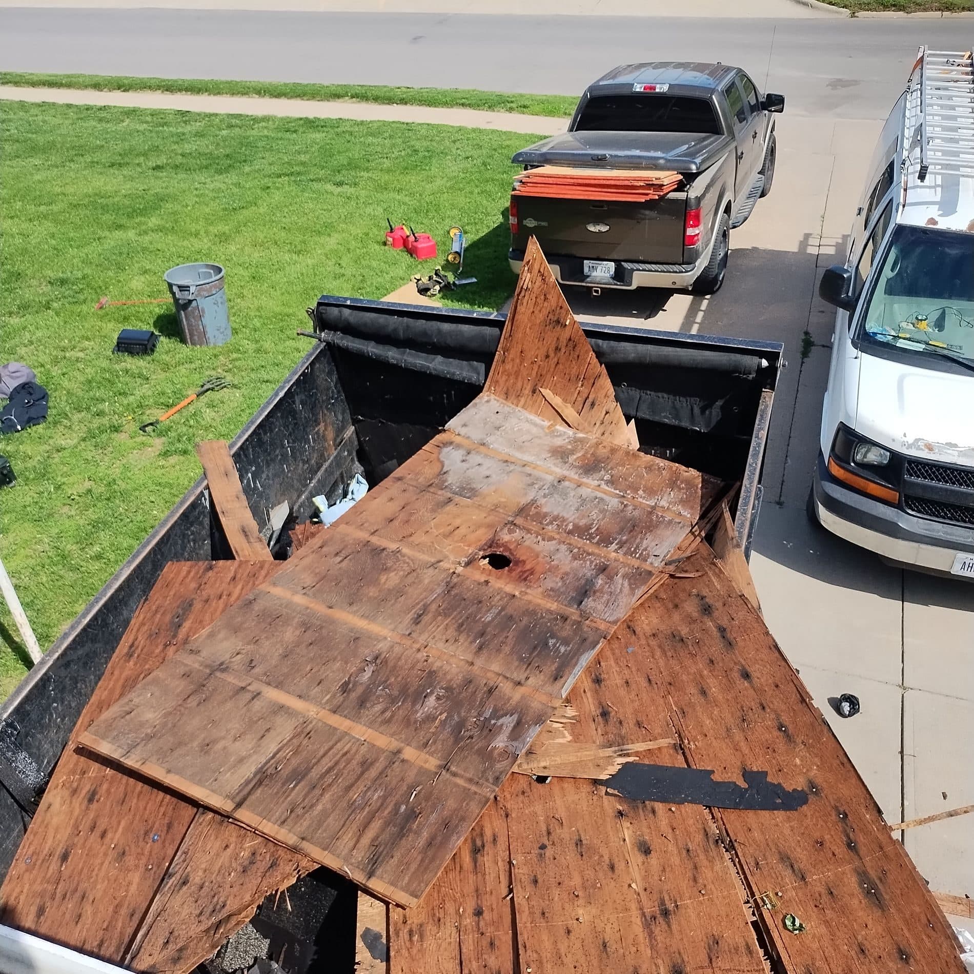 Looking down into a debris dumpster filled with old shingles beside work vehicles