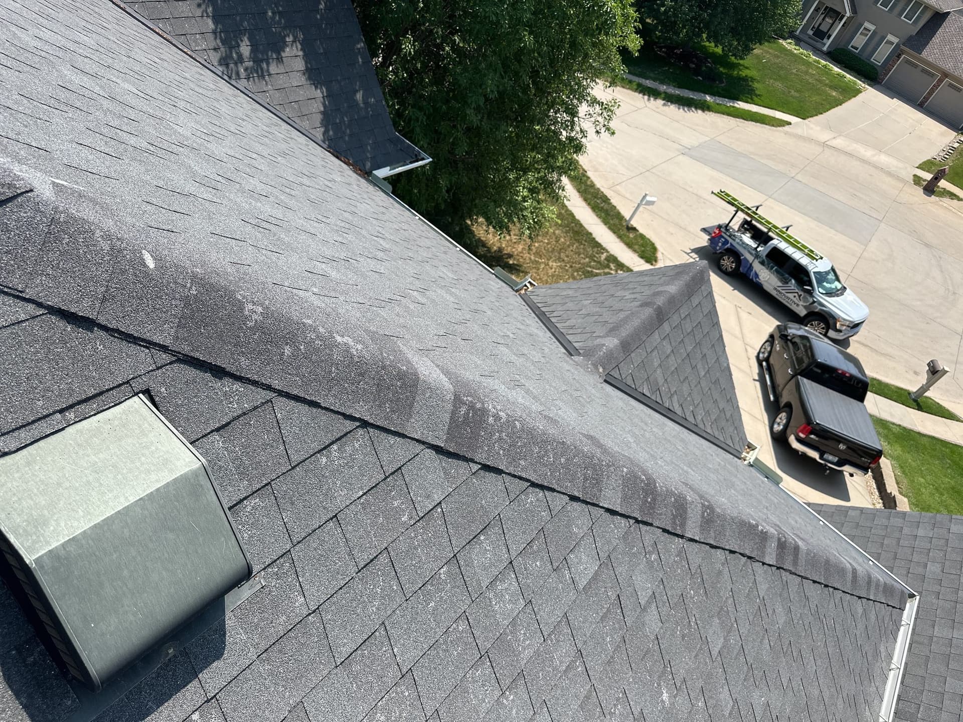Aerial-style view across new gray shingles with a roof vent and neighborhood beyond