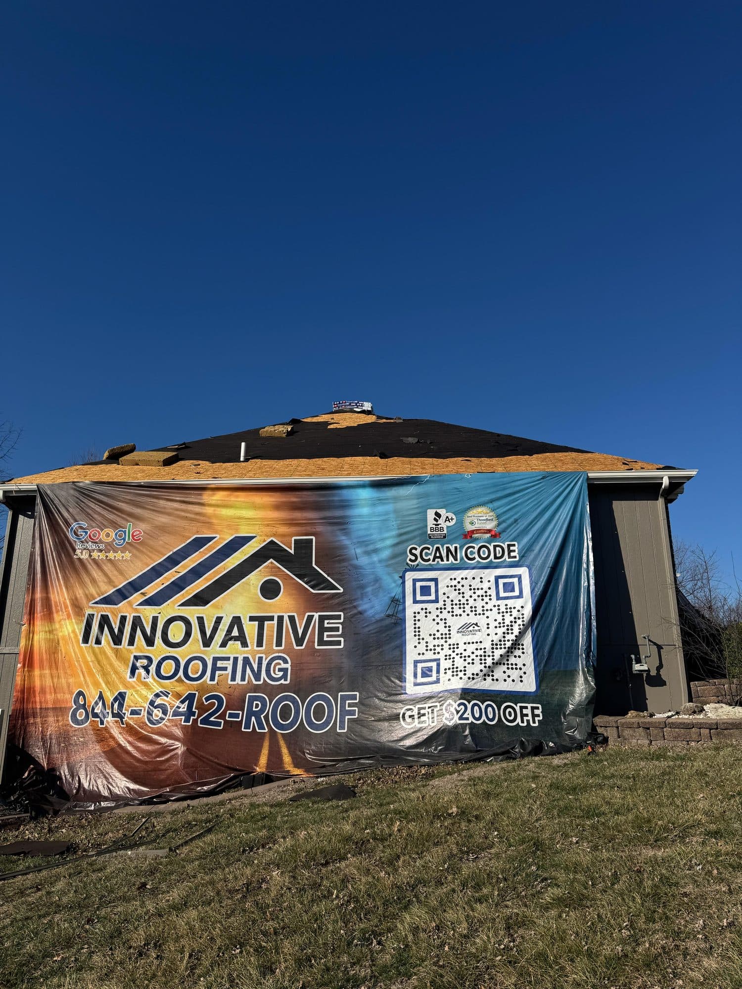 Two-story home with a large Innovative Roofing promotional banner covering the side during a roof replacement